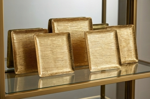 A single gold textured square plate holding a single macaron and a small olive oil bottle on a glass and gold room service cart.