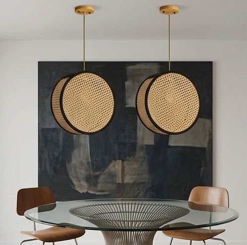 A round, illuminated pendant light made of woven natural rattan cane webbing with a black metal frame, hanging from a ceiling with a wood canopy.