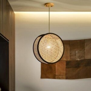 A round, illuminated pendant light made of woven natural rattan cane webbing with a black metal frame, hanging from a ceiling with a wood canopy.