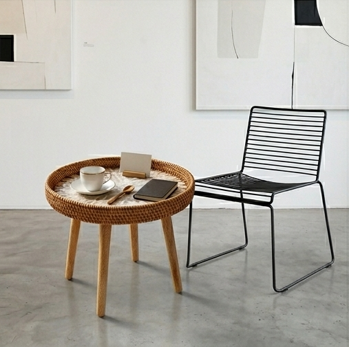 A round side table with three tapered light wood legs. The tabletop features a sunburst shell mosaic pattern in white and tan, surrounded by a raised edge made of woven natural rattan.
