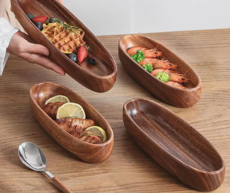 A multi-tiered wooden serving stand holding four empty, boat-shaped wooden bowls. The stand features a brass-toned plaque with the Verdequale VQ logo. The tableware is set on a wooden table alongside gold appetizer forks and an embroidered linen napkin.